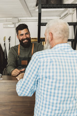 Smiling bearded hair stylist conversing with elderly client in salon