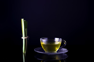 Chá de Erva Cidreira Fresca na chícara de vidro ao lado do ramo de folhas frescas de Cidreira na mesa de vidro espelhada com fundo preto