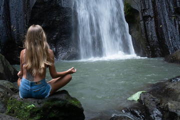 Aerial drone view back of woman meditating at the beautiful waterfall in green tropical rain forest in Bali, Indonesia