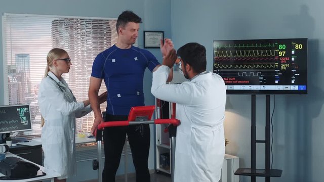 Doctors putting electrodes on sportsmas standing on racetrack in big modern lab with skyscrapers in the background