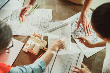 Top view of achitect-engineer's hands shows future house, office or store design plans to a young couple. Meeting at the construction office to talk about facade, interior decoration, home layout.