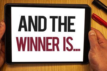 Handwriting text And The Winner Is . Concept meaning Announcing as first place in competition or race Hand hold showing colorful letters black marker red pen timber carrel