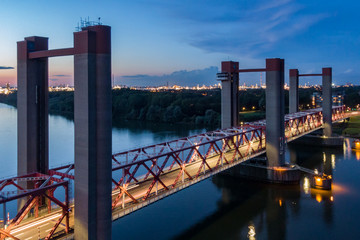 Aerial view of the Spijkenisse bridge over the river Maas at night. Illuminated traffic lane. Blue sky with sunset colors. Industrial lights of the Botlek and the city Hoogvliet in the distance. 