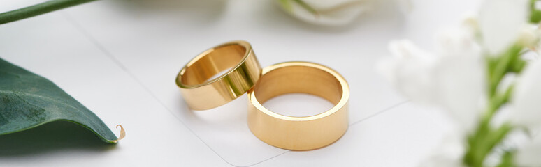 selective focus of golden wedding rings on white envelope, panoramic shot