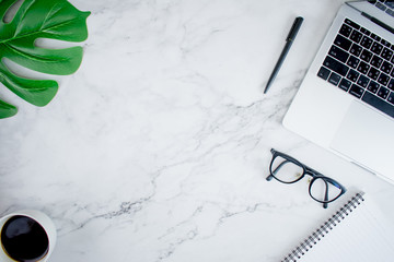 Modern marble office home office desk with laptop, leaf, glasses, coffee and accessories.Top view...