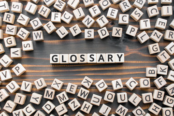 Glossary - word from wooden blocks with letters, alphabetical list with words meanings dictionary glossary  concept, random letters around, top view on wooden background