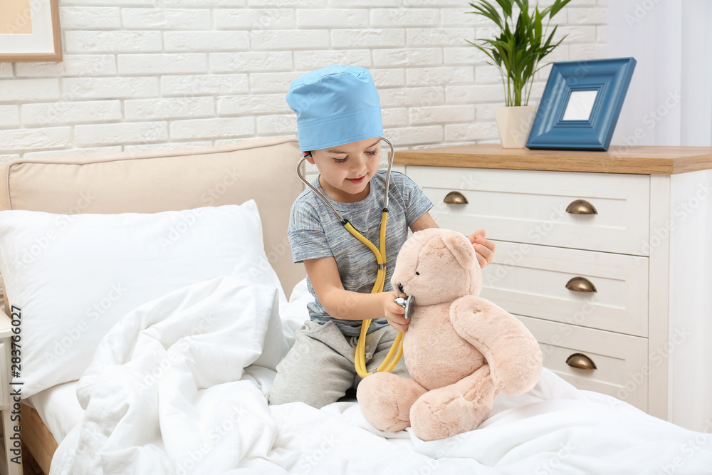 Wall mural cute child playing doctor with stuffed toy on bed in hospital ward