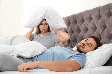 Upset young woman sitting on bed near her sleeping husband at home. Relationship problems