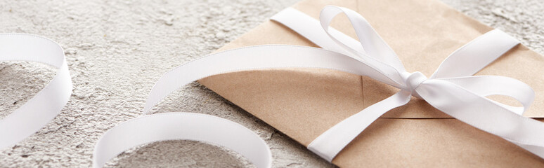 panoramic shot of beige envelope with white ribbon on textured surface