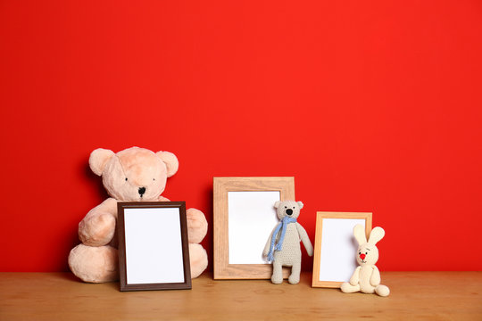 Soft toys and photo frames on table against red background, space for text. Child room interior