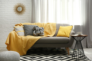 Stylish living room interior with soft pillows and yellow plaid on sofa