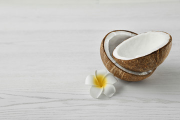 Fototapeta na wymiar Halves of coconut and flower on white wooden background. Space for text