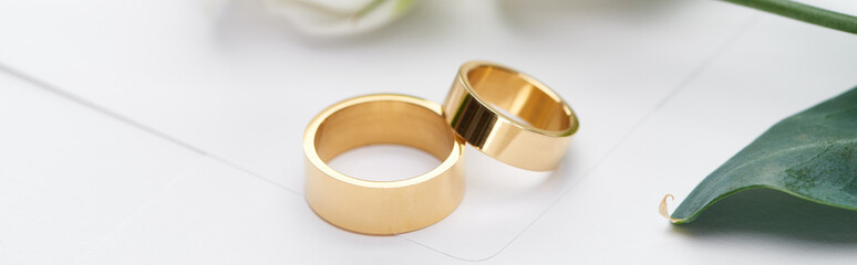 panoramic shot of golden wedding rings on white envelope