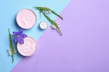 Flat lay composition with jars of body cream and flowers on color background. Space for text