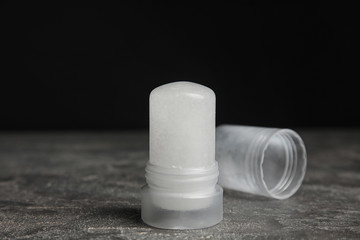 Natural crystal alum deodorant and cap on grey table against black background