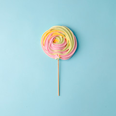 Colorful unicorn rainbow color meringue lollipop candy on pale on blue background. Flat lay. Summer sweet Minimal concept.