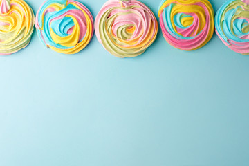 meringues in unicorn rainbow pastel colors, frame and copy space on blue backgound, simple minimal