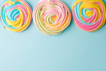 Fototapeta na wymiar meringues in unicorn rainbow pastel colors, frame and copy space on blue backgound, simple minimal