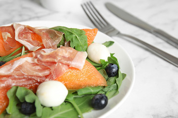 Fresh melon with prosciutto, mozzarella and arugula on plate, closeup