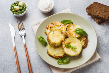 Slices of fried zucchini in batter with garlic and Basil on a plate.