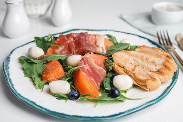 Fresh melon with prosciutto, mozzarella and arugula on white table