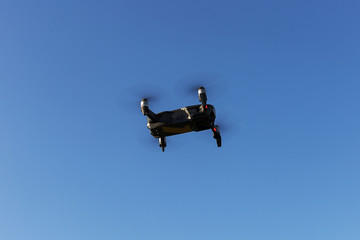 A drone, a quadrocopter with a camera for video shooting, flies against a blue sky.