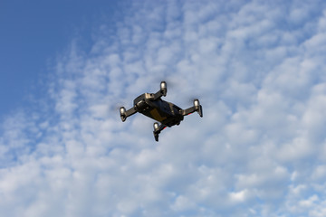A drone, a quadrocopter with a camera for video shooting, flies against a blue sky with clouds.