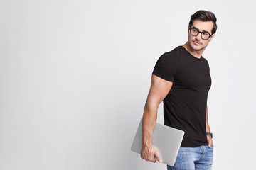 Handsome young man with laptop on grey background. Space for text