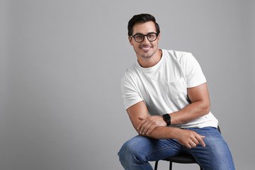 Handsome young man sitting on stool against grey background. Space for text