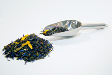 a metal spoon with dry tea leaves lies next to a bunch of tea leaves