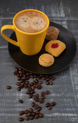Taza amarilla de cáfe en plato negro con granos de café