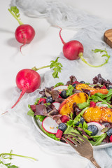Fresh spring salad with rucola, lettuce, blueberries, radish, beet and slices of peach. White background with free text space