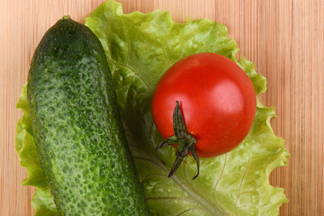 Ripe tomato and cucumber on a lettuce leaf on top of a wooden background.