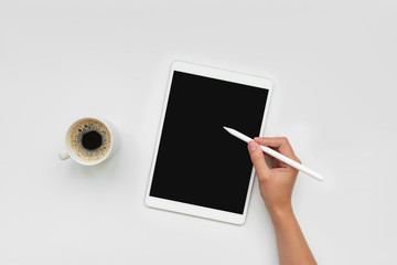 Cup of coffee and feminine hands drawing on tablet by pencil on white desk. Top view. Copy space. Mock-up