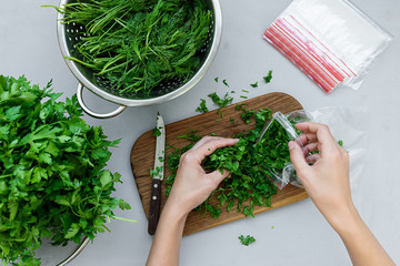 Feminine hands poured into disposable package chopped fresh green parsley and dill or fennel on gray wooden table. Top view. Copy space. Harvesting concept
