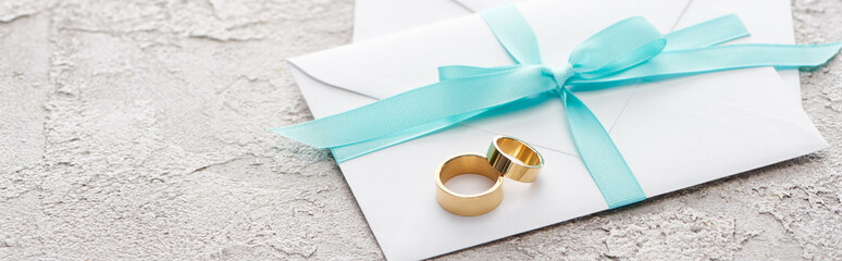 panoramic shot of golden rings on white envelope with blue ribbon