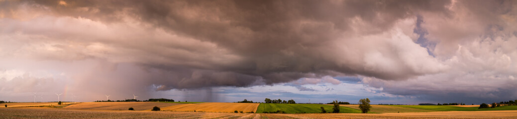 Thunderstorm clouds with rain and rainbow over the fields, panorama 