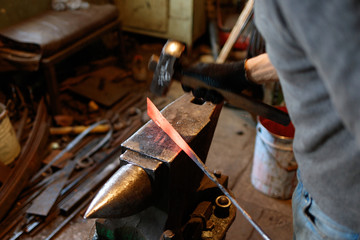 Blacksmith forging red-hot metal with hammer.