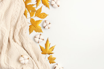 Flat lay autumn composition. Knitted woolen light beige sweater or plaid, golden dry leaves, cotton flowers on white background top view copy space. Autumn, fall concept