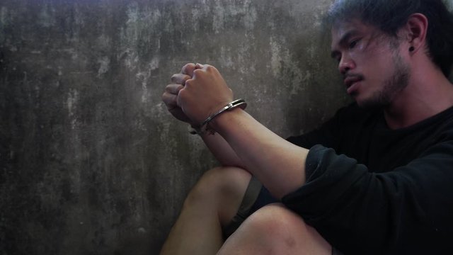 Prisoner young man get depressed and thinking about future life. Thief guy is cuffed and sit in jail at police station before sending to prison. He look guilty and sadness. Asian young man is murderer