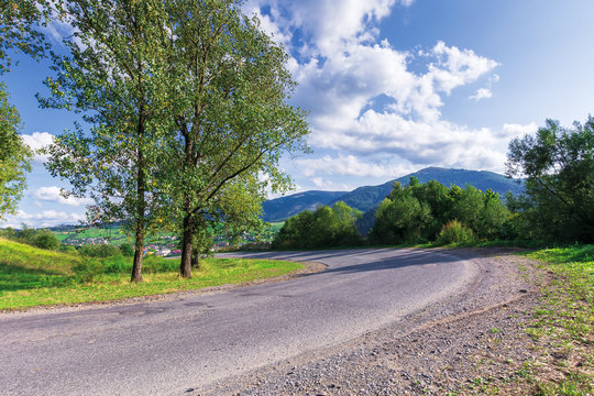 serpentine road in mountains. beautiful scenery in evening light. wonderful september weather with fluffy clouds on the sky. trees on grassy meadow along the path. range in the distance