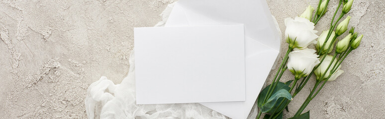 panoramic shot of empty invitation card on white cheesecloth near eustoma flowers on textured surface