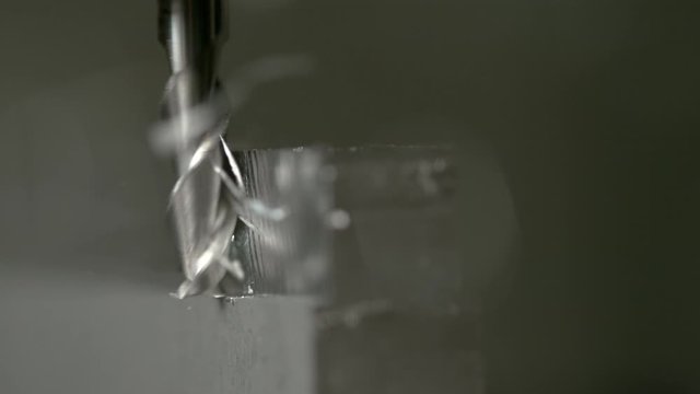 SLOW MOTION, MACRO, DOF: Detailed close up shot of a fine end mill shaving the side of a matt block of metal. Small twisted shavings come flying off an aluminium workpiece processed by lathing machine