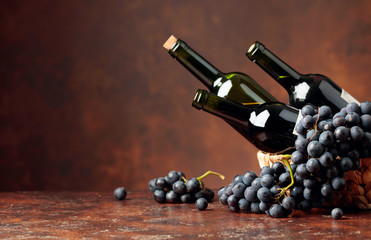 Juicy blue grapes and bottles of red wine on a brown background.