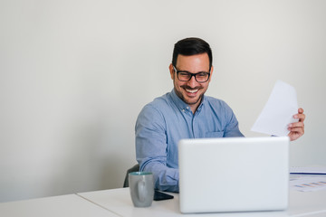 Young smiling cheerful businessman in office working with laptop computer