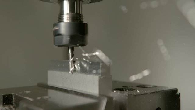 SLOW MOTION, MACRO, DOF: Shiny chips of metal come flying off a workpiece during end milling. Sharp cutter spinning and shaving the side of a matt block of aluminium. Conventional metalwork method.