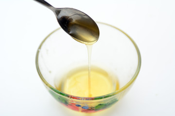 Liquid honey is poured from a teaspoon into a transparent cup. Concept - Healthy Eating