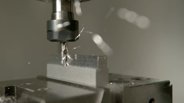 SLOW MOTION, MACRO, DOF: Sharp industrial drill spinning and end milling a matt piece of aluminium. Automated lathing equipment processing a workpiece during the end milling process. Shavings flying