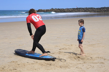 Leçon de surf à un jeune garçon sur la plage avec un instructeur