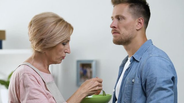 Patient man submissively eating with spoon to please his mother, relationship